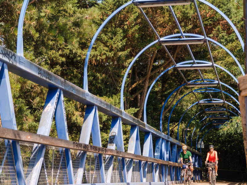 Deux cyclistes traversent la passerelle métallique bleue de la coulée verte du sud parisien, voie verte de la Véloscénie au départ de Paris.