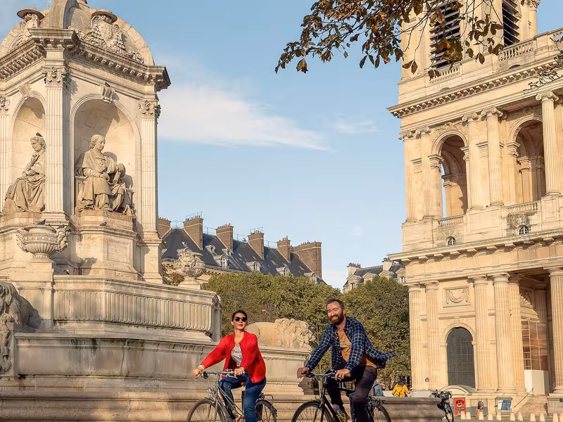 Deux cyclistes place Saint-Sulpice à Paris, devant la fontaine et l'église, au départ de la Véloscénie Paris-Mont-Saint-Michel.
