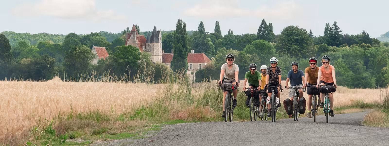Cyclistes roulant sur une route avec vue du manoir de la Vôve en arrière-plan