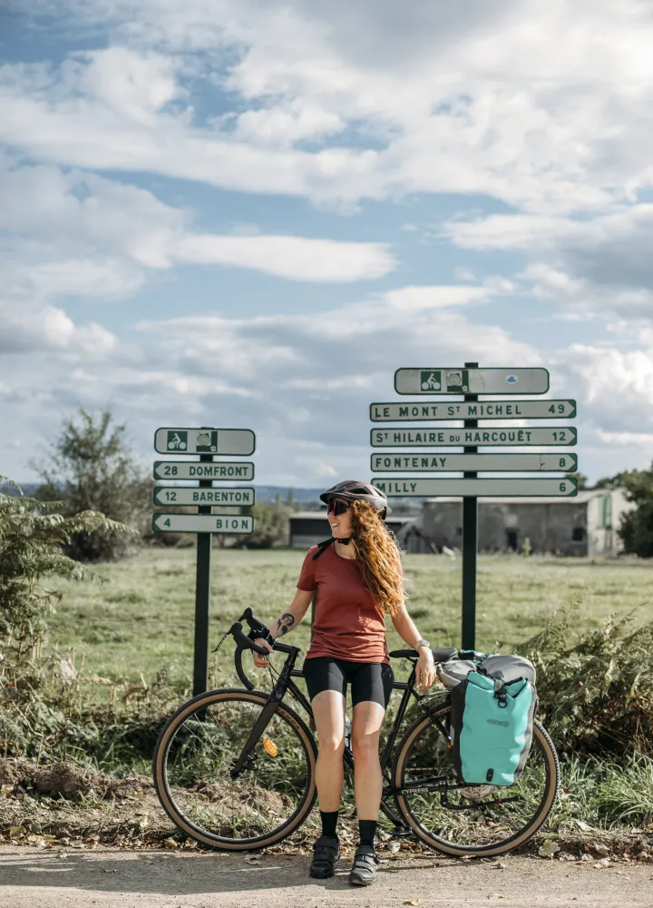 Cycliste et vélo de voyage devant un panneau voie verte Le Mont-Saint-Michel sur la La Véloscénie