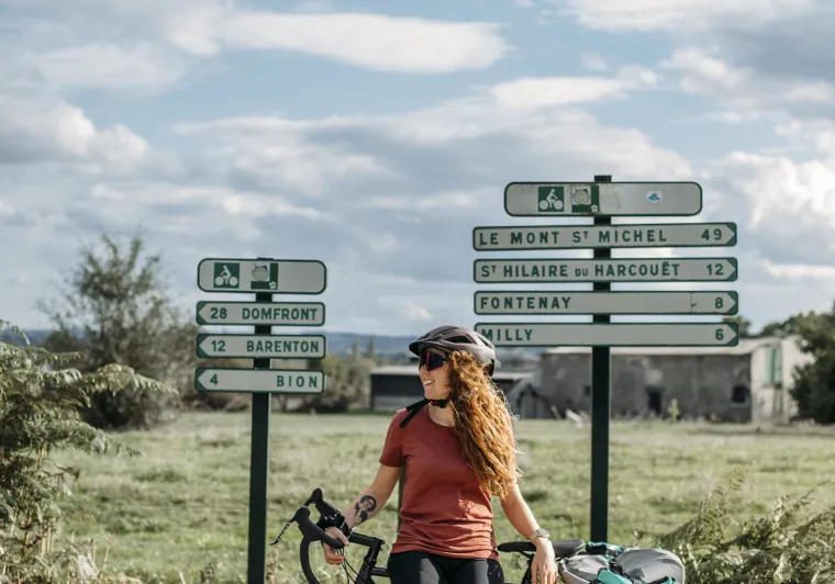 Cycliste et vélo de voyage devant un panneau voie verte Le Mont-Saint-Michel sur la La Véloscénie