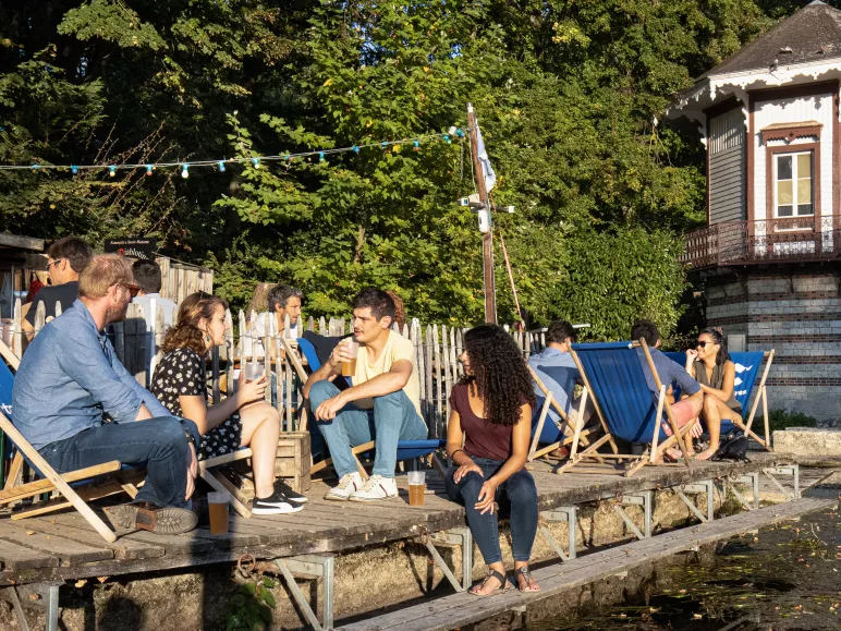 Des personnes assises dans des transats prennent un verre au bord de l'eau à la guinguette de Chartres.