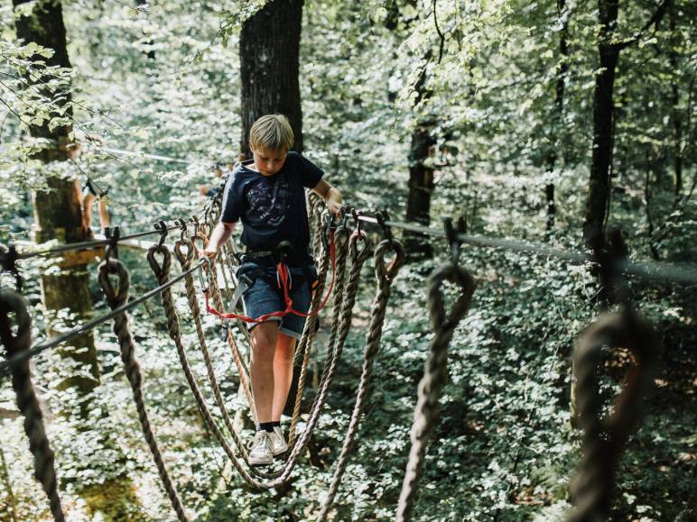 Un garçon traverse un pont de singes en hauteur dans l'accrobranche de Bagnoles de l'Orne