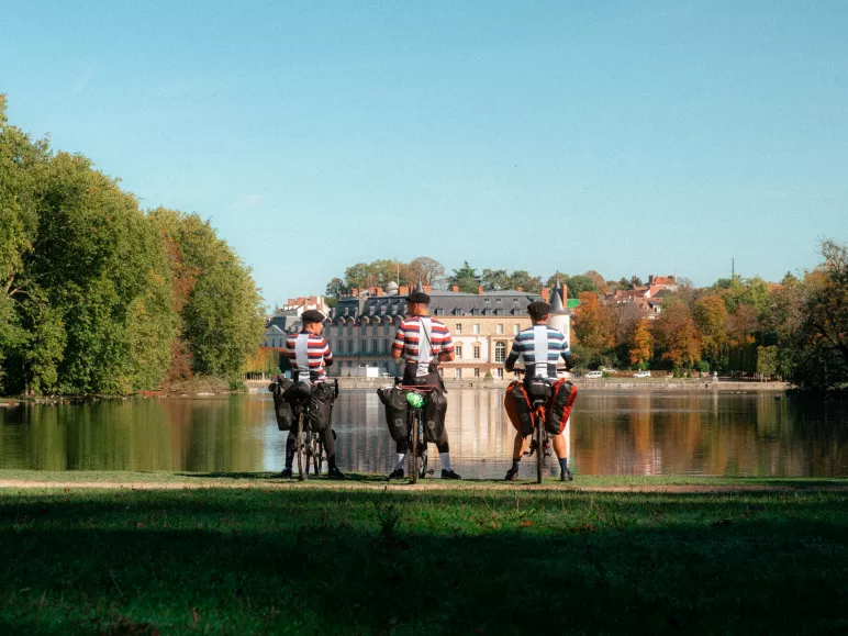3 cyclistes regardent le château de Rambouillet se refléter dans le canal